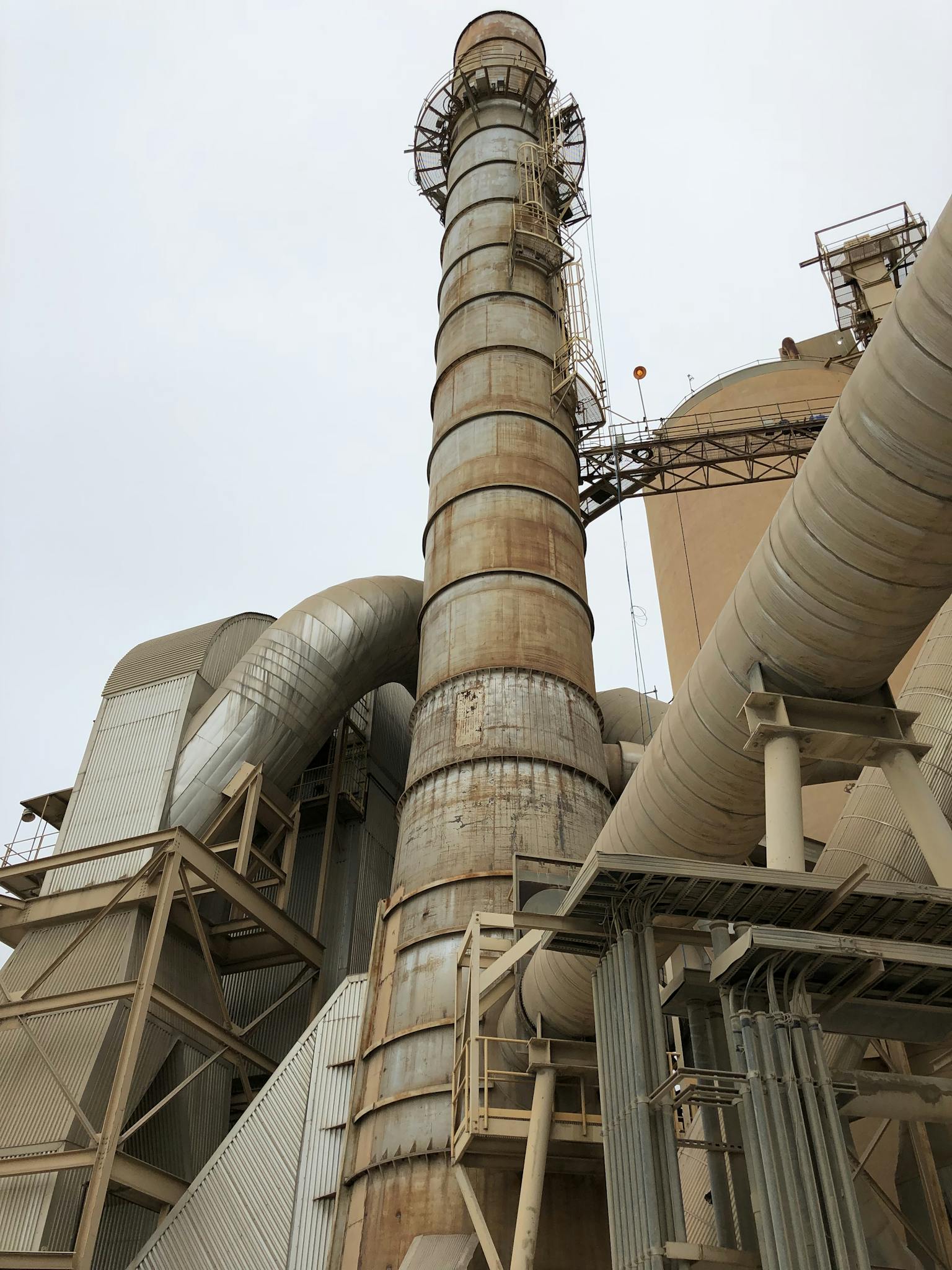 Close-up of a large industrial factory chimney and pipes against the sky, showcasing infrastructure.